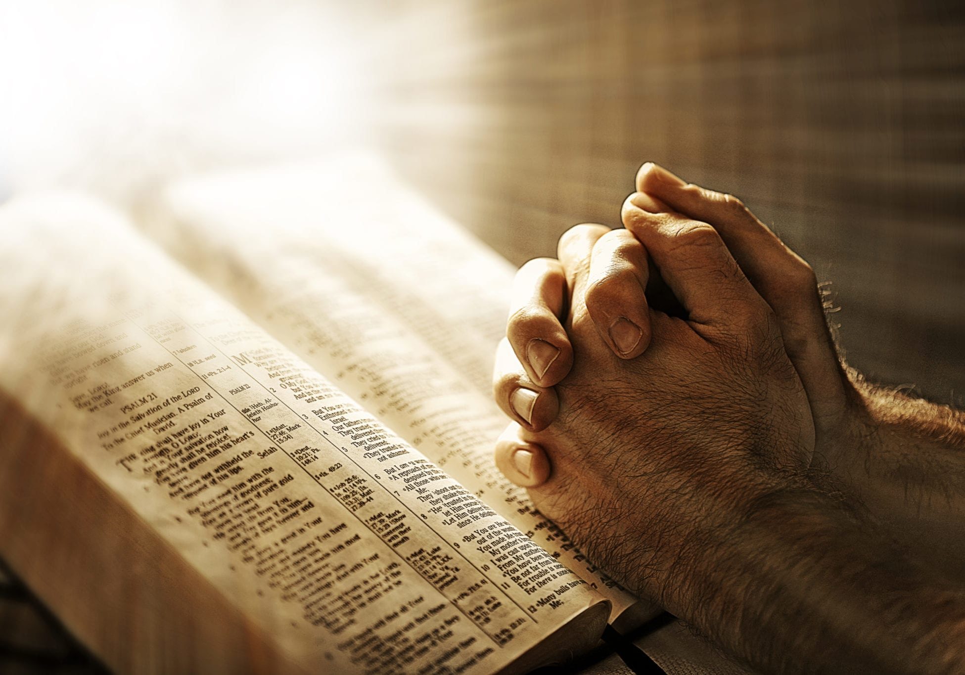 Two hands are in prayer while resting on the Bible